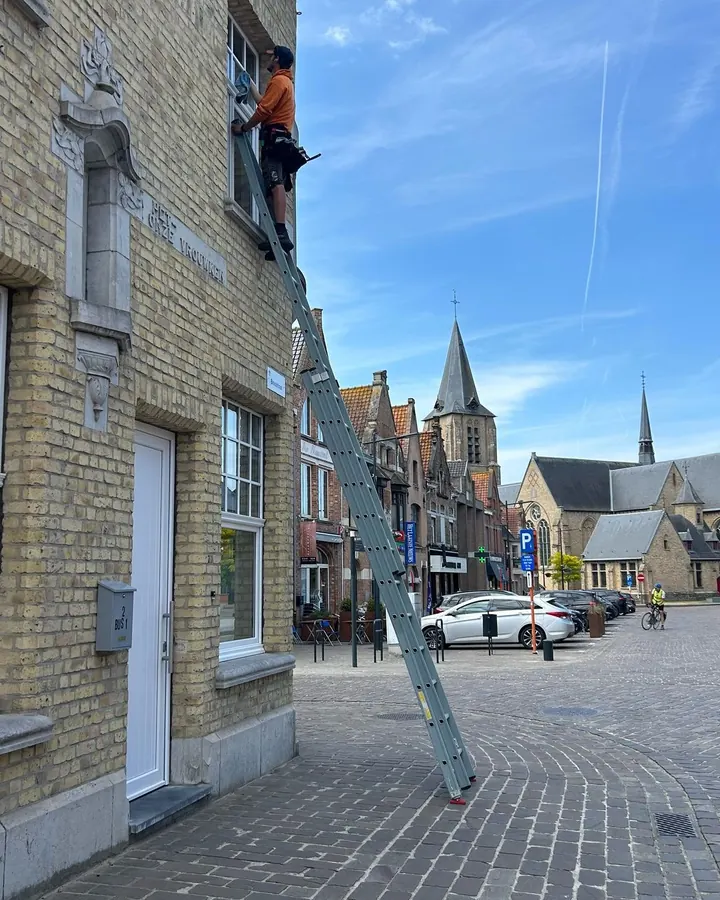 Kjell wast de ramen van een gevel vanop een ladder
